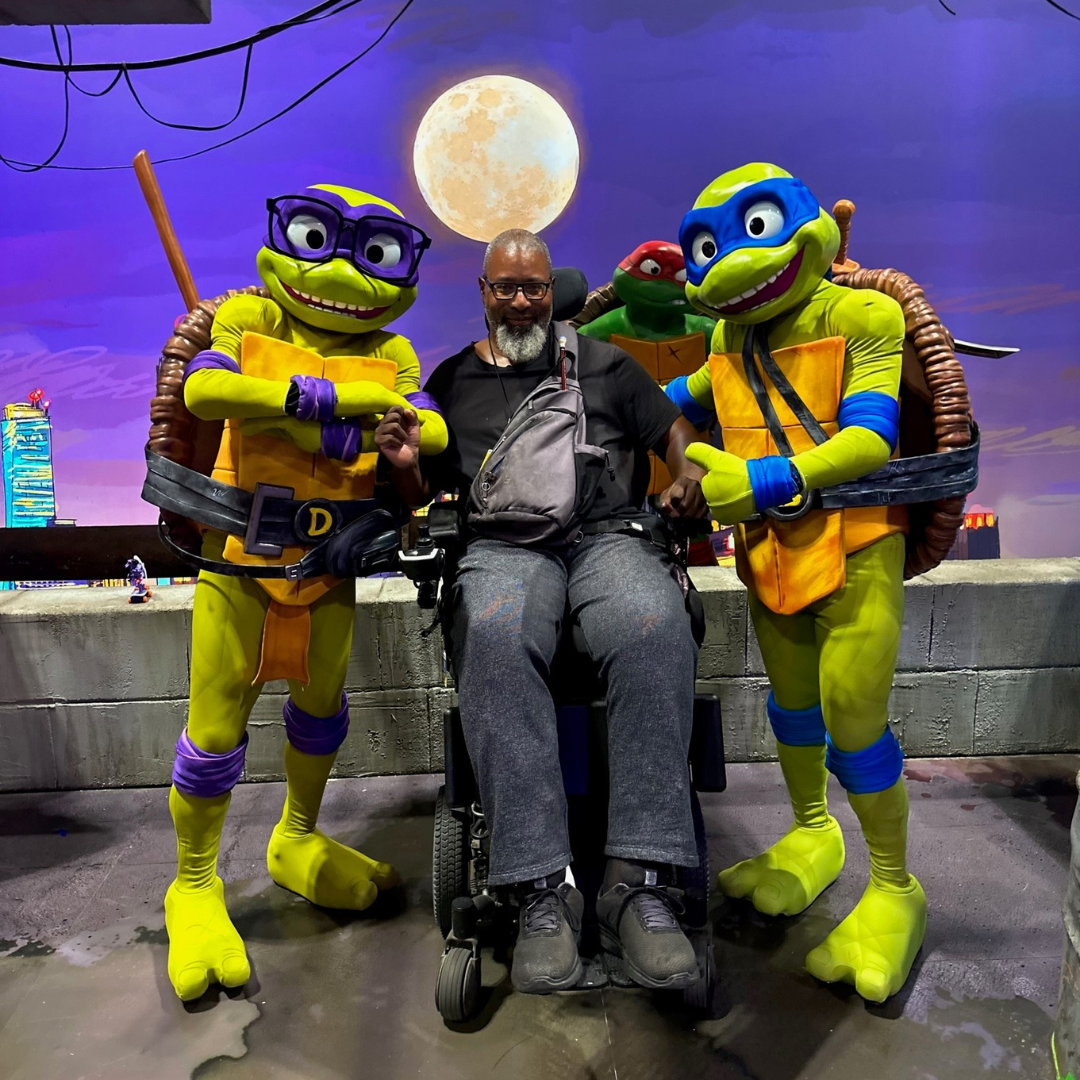 Garrick standing next to two people dressed at Ninja Turtles.