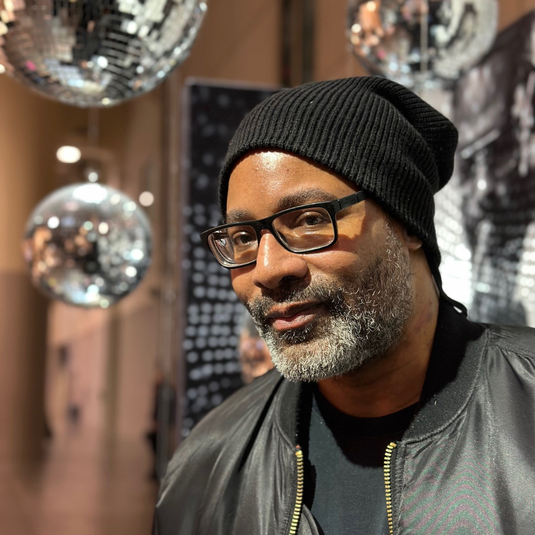 A close up of Garrick in front of disco balls. He is wearing a black hat.
