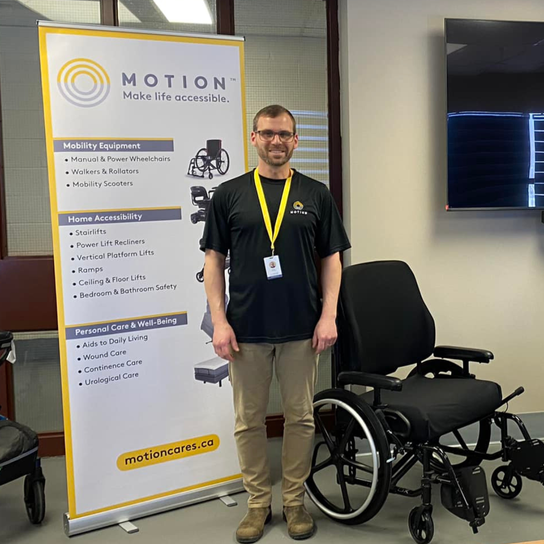 Motion Employee pictured with product offering banner on left and manual wheelchair on right.
